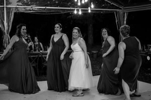 Wedding party dancing in formal attire under a tent during an evening reception celebration.