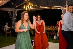 Wedding guests in burgundy and green dresses dance under tent with string lights.