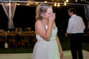Someone in a white dress reacts emotionally during what appears to be an outdoor evening wedding reception.