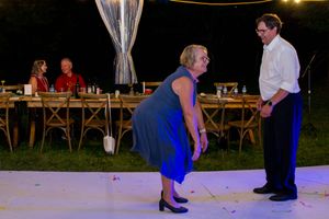 People dancing on an outdoor dance floor at night with rustic wooden tables and chairs in the background.