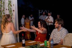 People enjoying drinks and conversation at a casual gathering with wine bottles and beverages on the table.