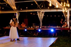 A couple dances together on an illuminated outdoor dance floor under string lights at a romantic evening event.