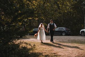 A couple walks hand in hand down a sunlit path during their wedding day.