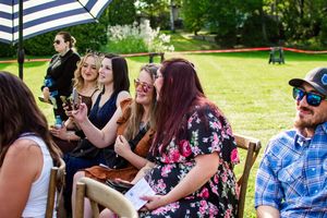 Wedding guests enjoy an outdoor reception under a striped umbrella on a sunny day.