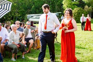 Wedding guests gather on a lawn with striped umbrellas and red dresses creating a festive atmosphere.