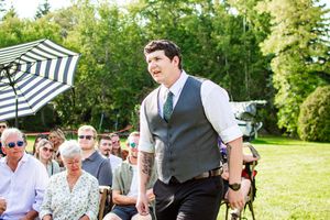 Wedding guests enjoy an outdoor reception under striped umbrellas on a sunny day.