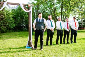 Wedding party members stand in a line on a grassy lawn during an outdoor summer celebration.
