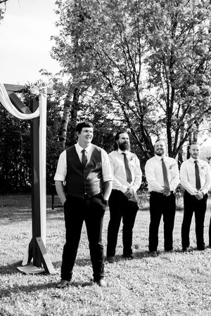 A black and white photo of groomsmen lined up outdoors with trees in the background.