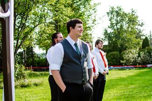 Groomsmen pose together on green grass with trees in the background at an outdoor wedding.