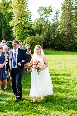 Wedding party walks across a sunny green lawn during an outdoor ceremony.