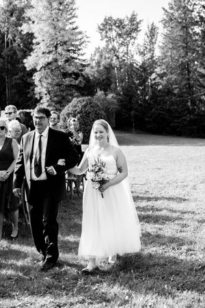 Wedding party walks across a grassy field during an outdoor ceremony in black and white.