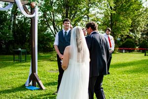 Outdoor wedding ceremony setup with white fabric draped posts and green natural backdrop.