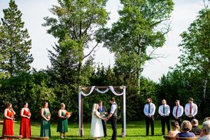 Outdoor wedding ceremony setup with white draped poles and wedding party on green lawn.