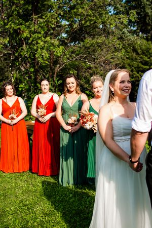 Wedding party wearing vibrant orange and green dresses poses together on a sunny lawn.