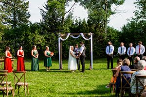 Wedding guests seated in rows on a grassy lawn with evergreen trees in the background.