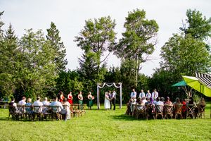 Wedding ceremony setup on a grassy hilltop with guests gathered under trees.
