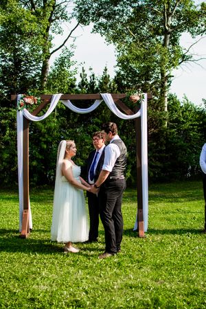Wedding ceremony in progress under white draped poles on sunny green lawn.