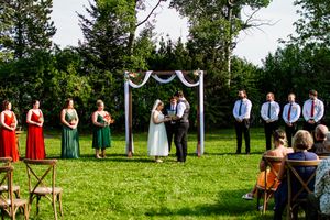 Panoramic view of outdoor wedding ceremony with white arch and rows of chairs on green lawn.