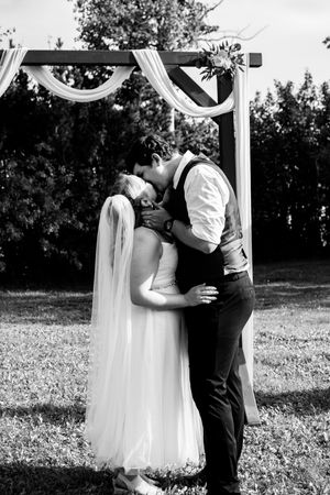 Black and white wedding photos of a couple embracing under an outdoor arbor in a garden setting.