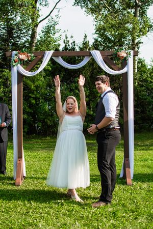 A joyful celebration under a white-draped wooden arch during an outdoor garden wedding ceremony.