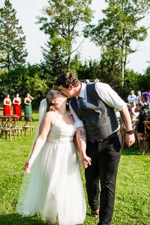 Couple sharing playful moment during outdoor wedding ceremony on grassy field.