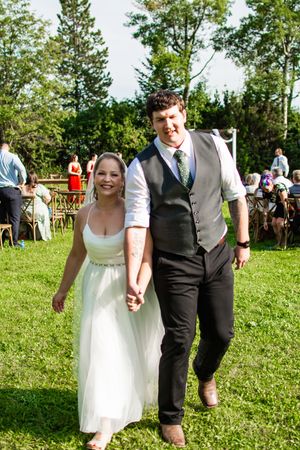Wedding party walks together across a sunny lawn during an outdoor summer celebration.