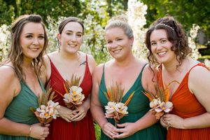 Wedding party members in alternating green and rust colored dresses holding bouquets outdoors.