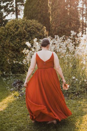 Flowing orange bridesmaid dresses twirl in golden evening sunlight against a natural backdrop.