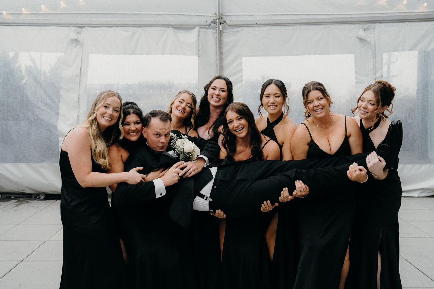 A group wearing black formal dresses poses together laughing and having fun at an event.