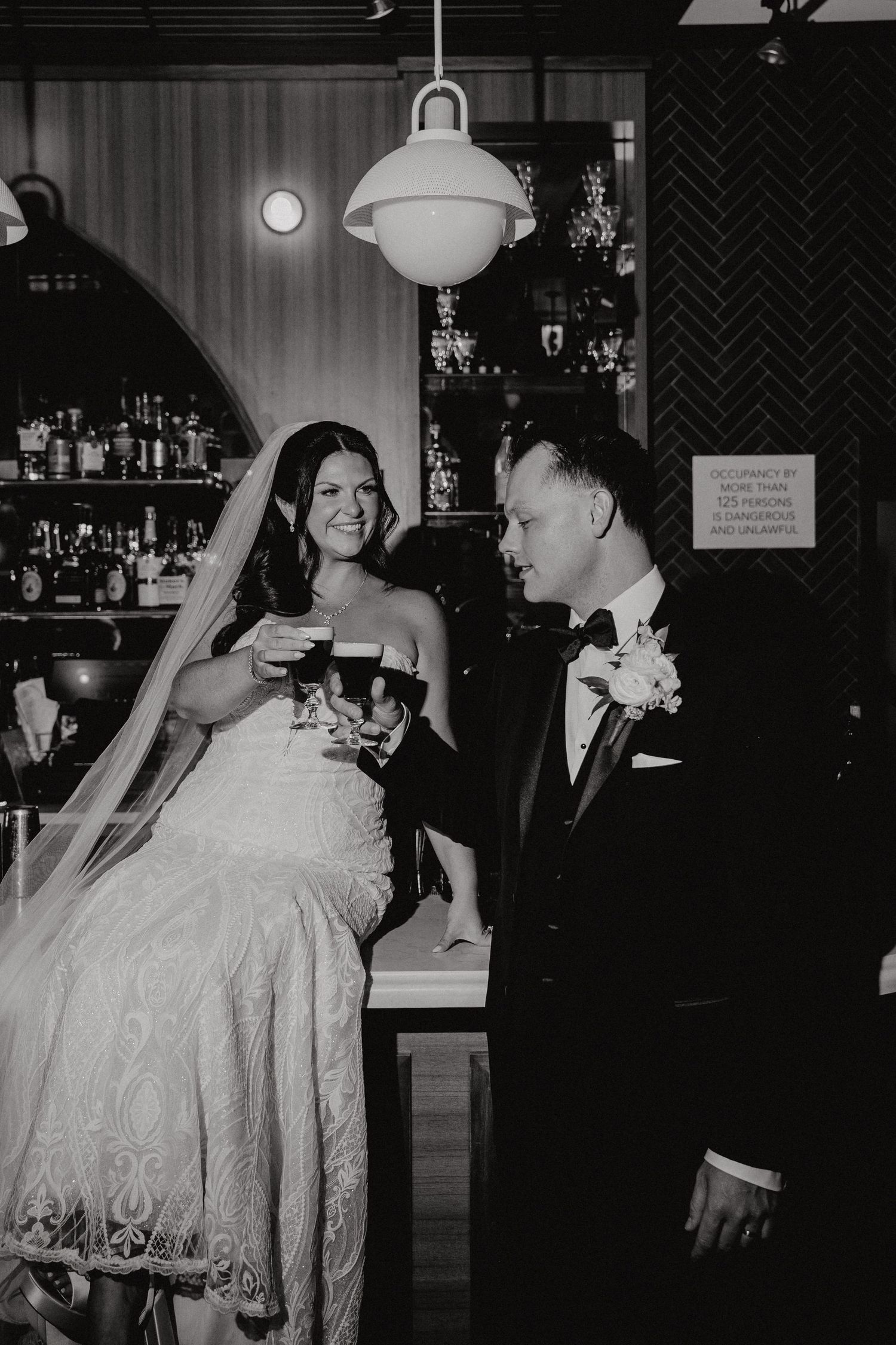 A bride and groom share a joyful moment laughing together during their wedding reception in a dimly lit venue.