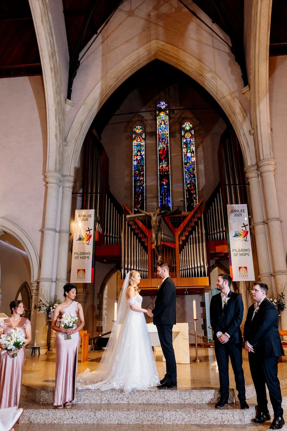 Wedding ceremony unfolds in a traditional church sanctuary with stained glass windows and organ pipes as backdrop.