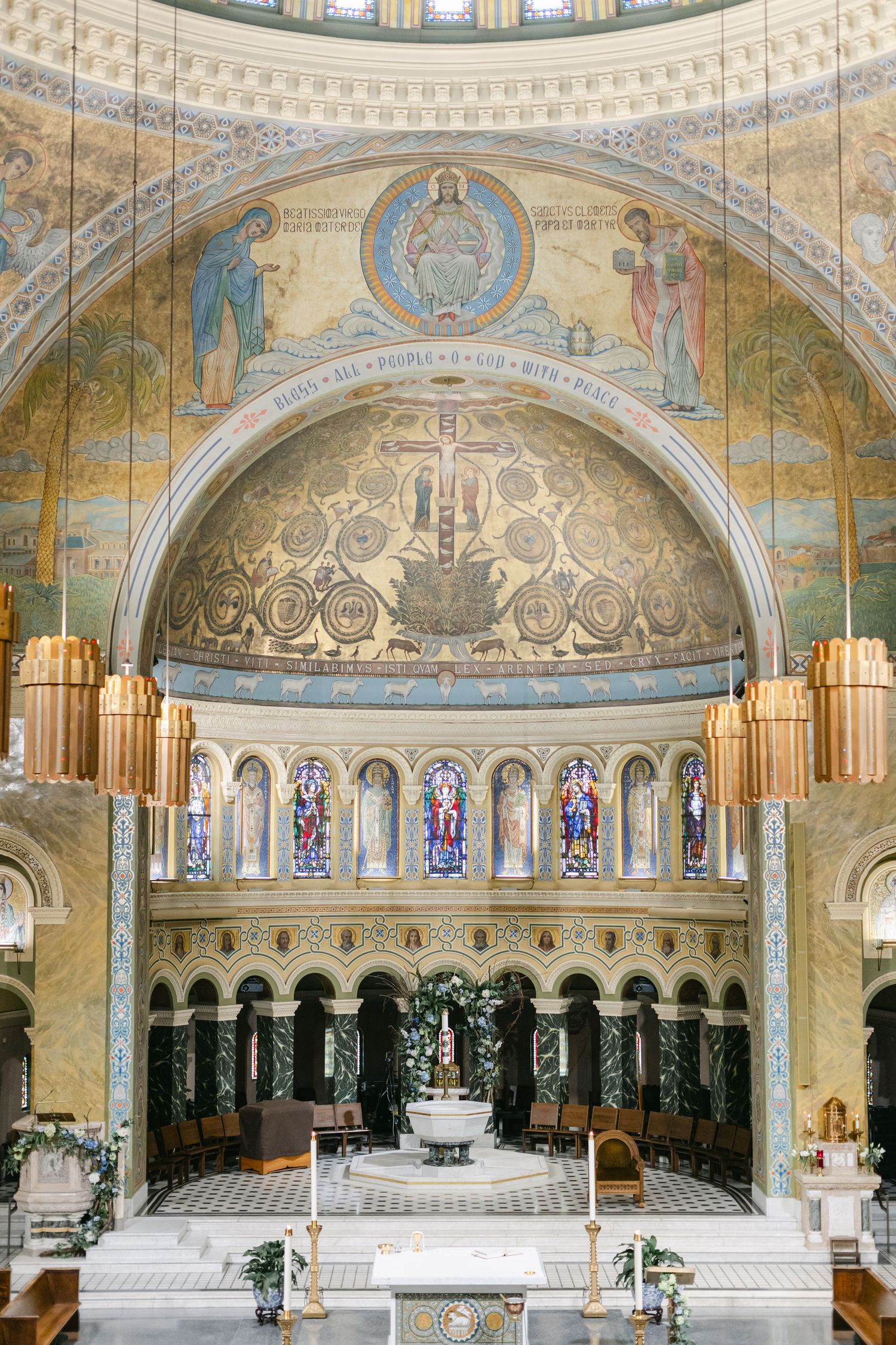 Interior view of ornate church sanctuary with golden mosaic domes, marble altar, and stained glass windows.