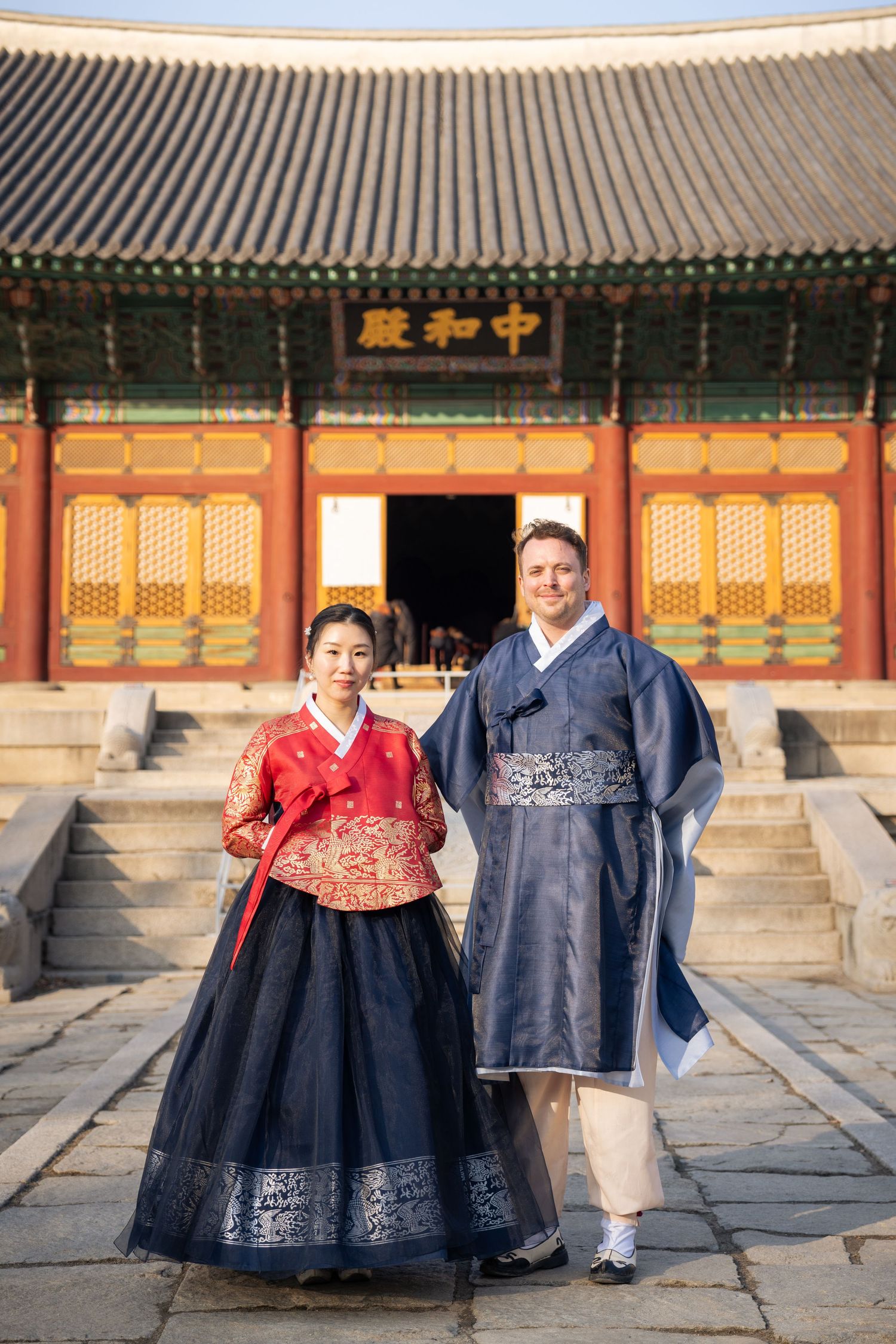 Traditional Korean hanbok outfits worn at a historic temple with ornate architecture in the background.