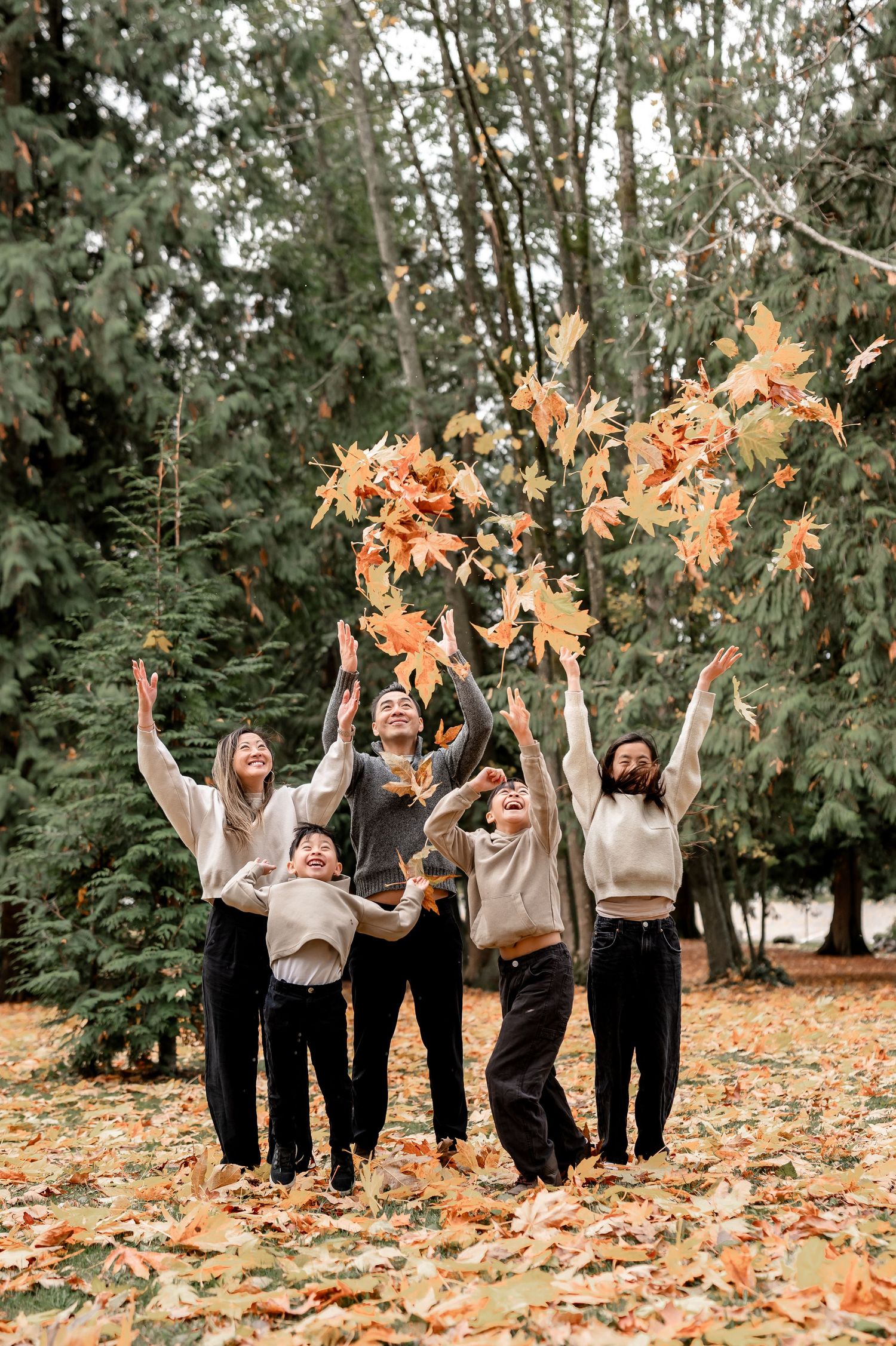 A group of people in coordinated outfits toss autumn leaves in the air while celebrating in a wooded outdoor setting.