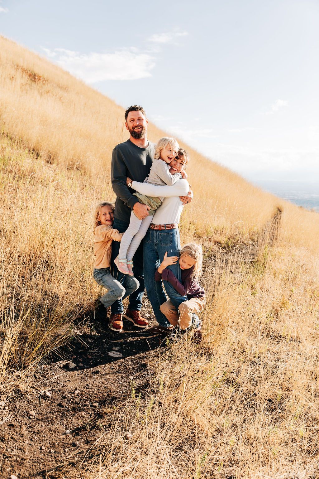 A family stands together on a golden hillside trail during sunset, surrounded by dry grass and mountain views.