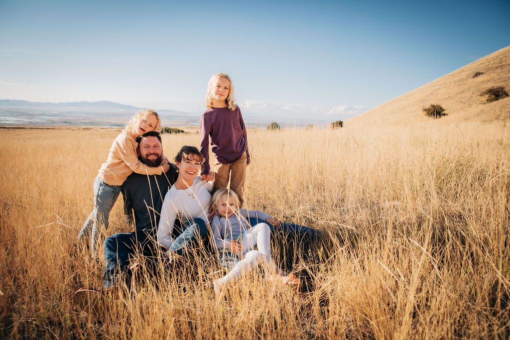 Family enjoying a warm sunset in tall golden grass on a hillside during an outdoor photoshoot.