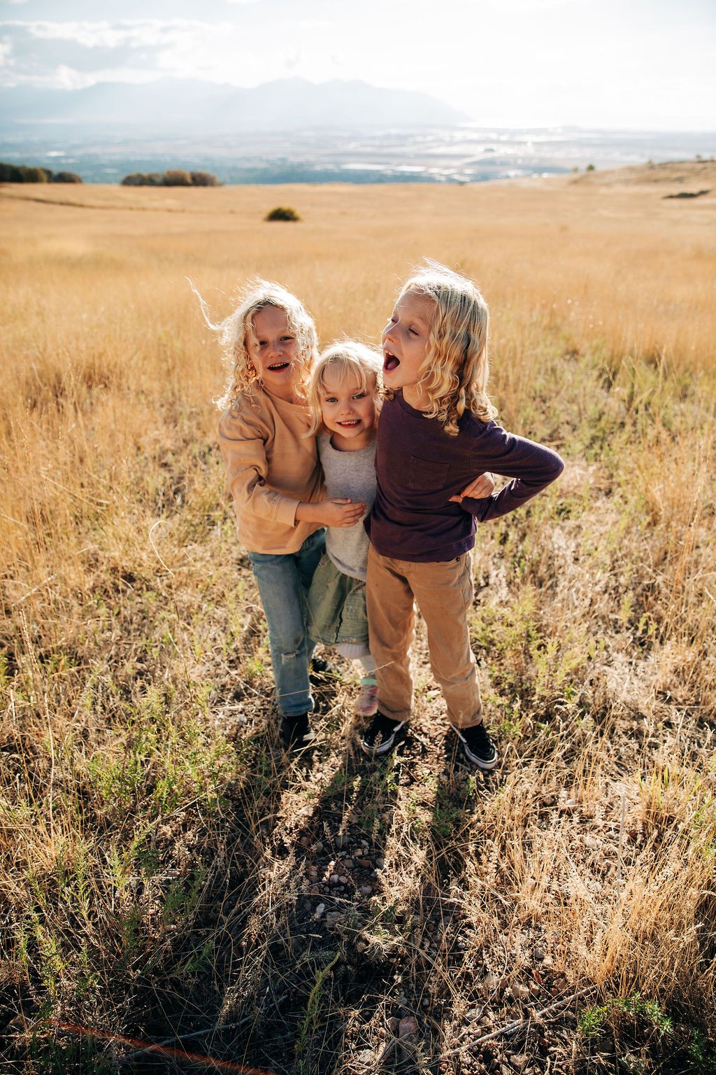 Family members laughing and hugging together in a golden field of tall grass during sunset.