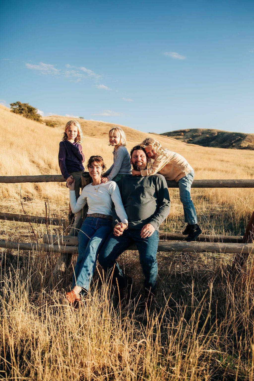 Family enjoying a playful moment together in a sunlit field with rolling hills.