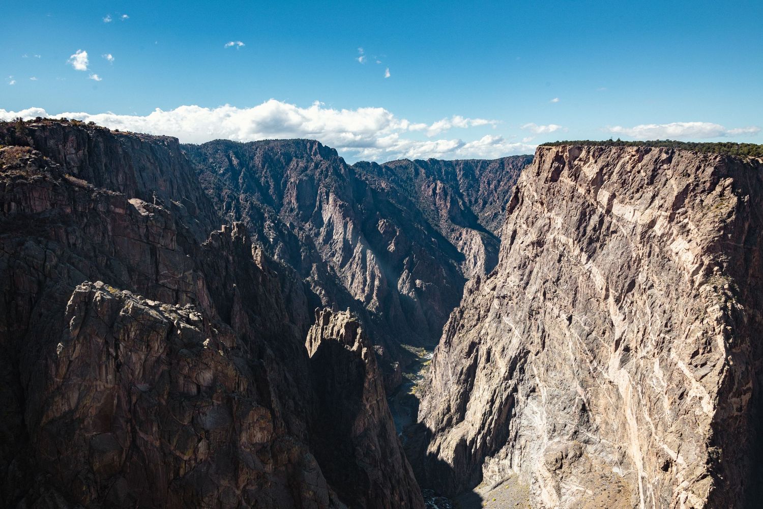 Panoramic view of steep canyon walls and cliffs in Black Canyon of the Gunnison National Park under blue skies.
