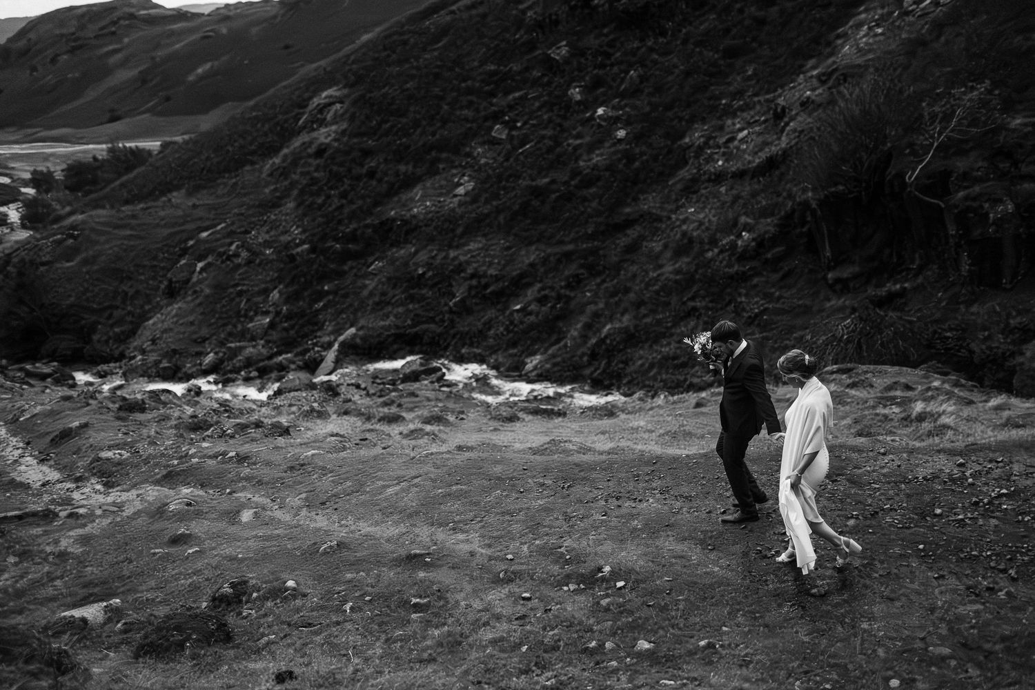 Chris and Christina walk down Coniston Old Man a dramatic mountain landscape with winding roads and rugged terrain in moody overcast weather