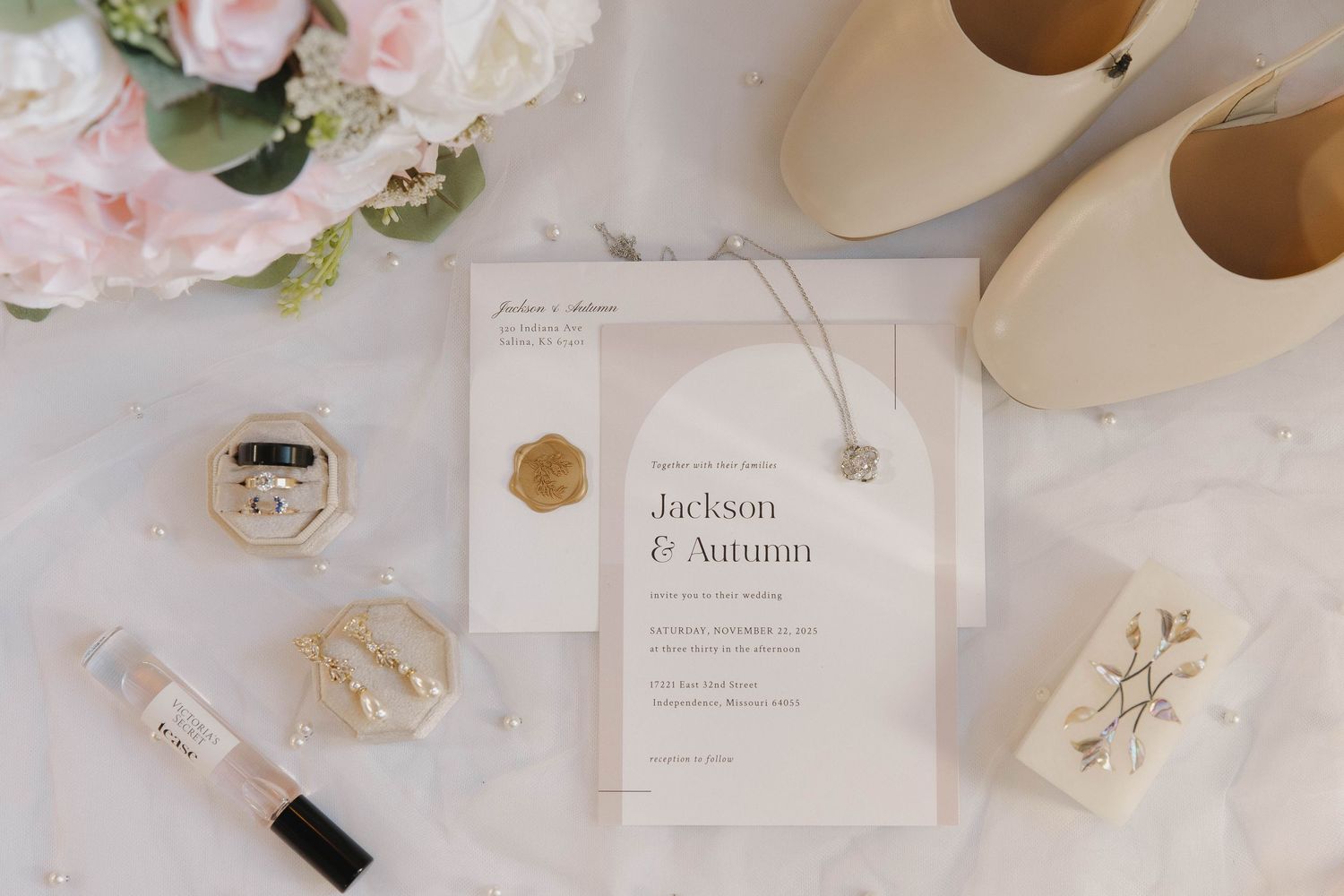 Elegant wedding invitation with floral details surrounded by pink roses, ballet flats, and delicate accessories on white surface.
