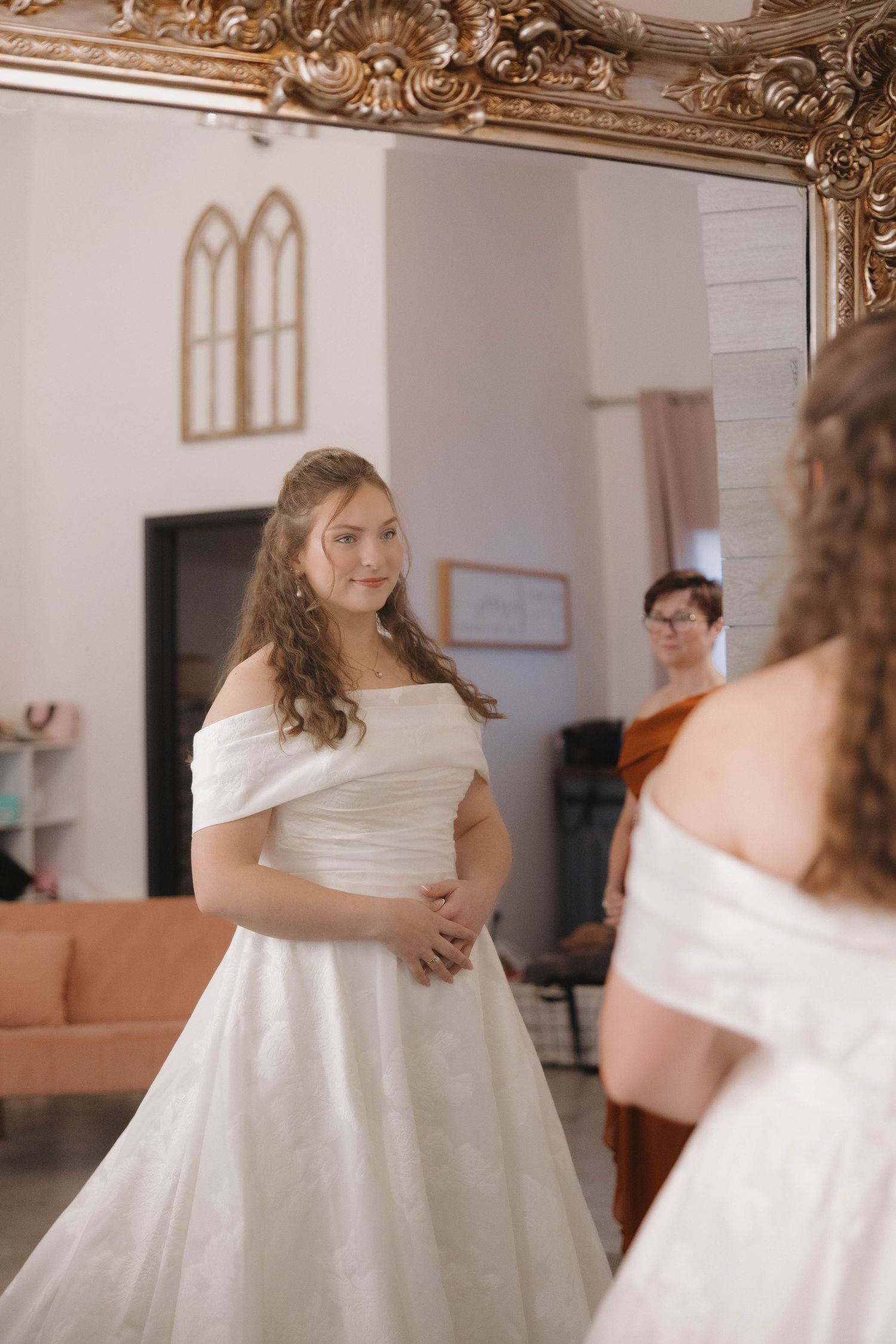 A bride in a white wedding dress twirls and dances in an elegant room with an ornate gold frame on the wall.