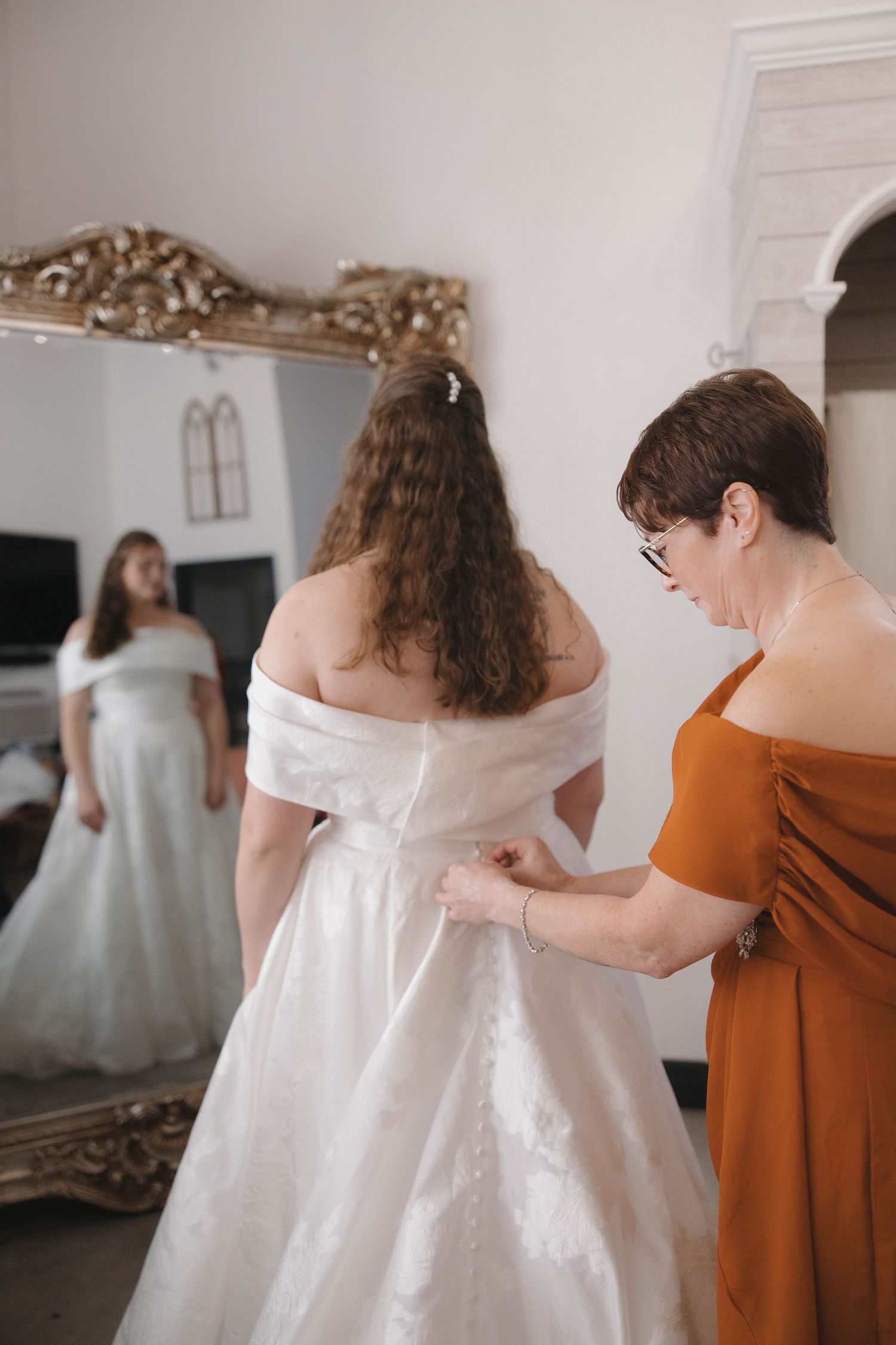 People helping with wedding dress preparations in a bright white room.