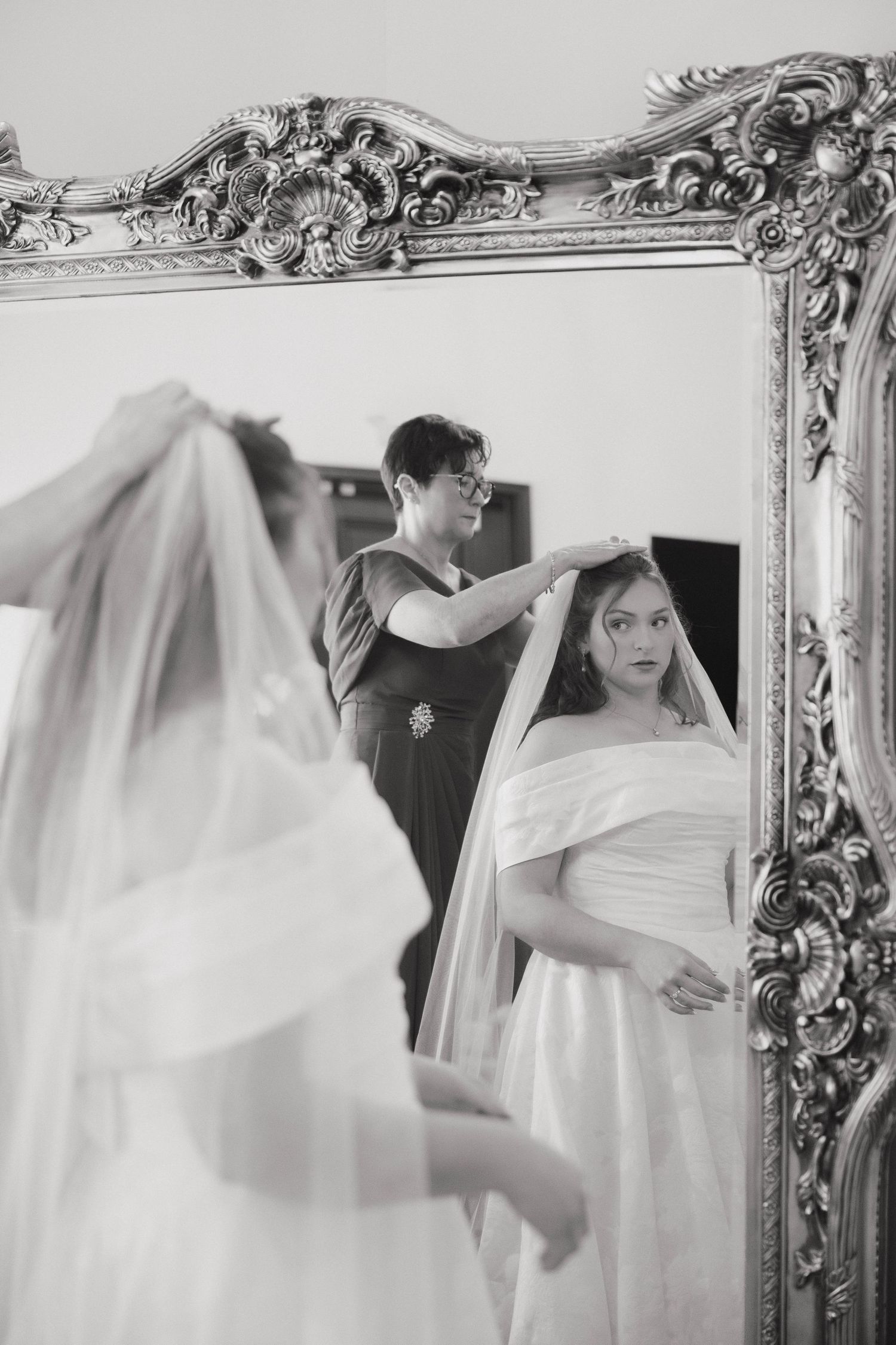 A reflection in an ornate silver mirror shows final adjustments being made to a wedding veil.