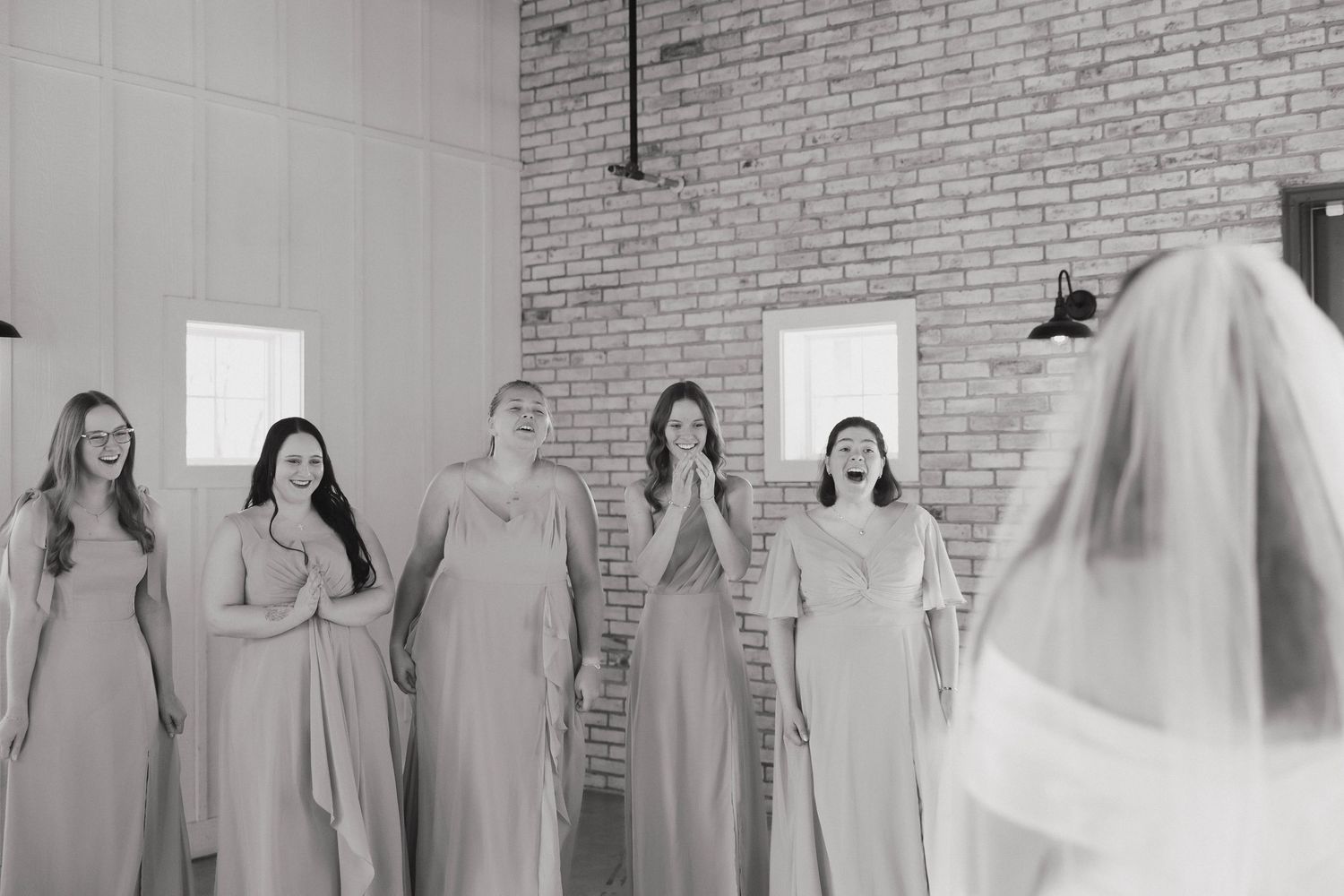 A panoramic black and white photo showing a wedding party standing in a row against a brick wall.