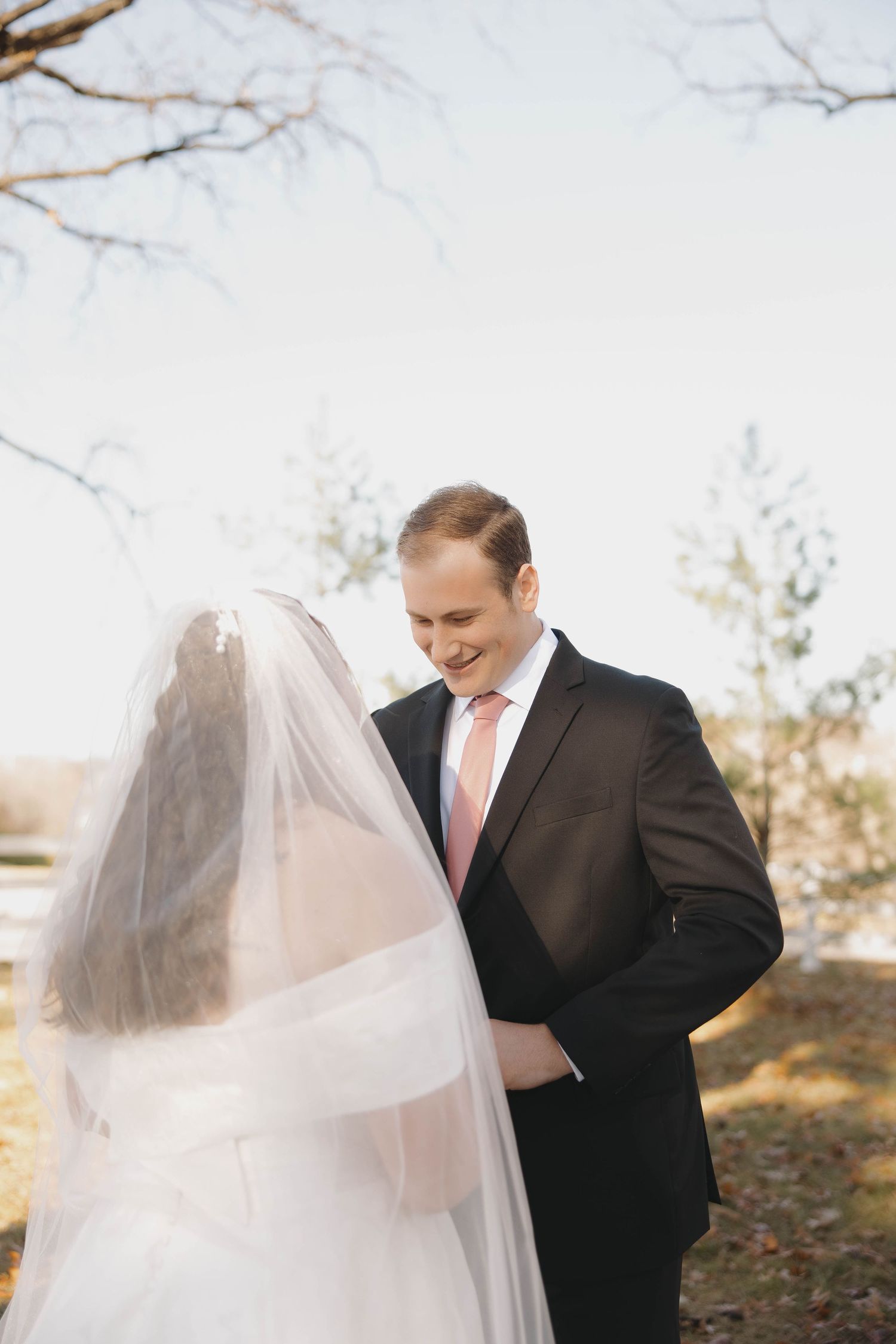 A romantic outdoor wedding moment captured between a bride in white veil and groom in dark suit during autumn.