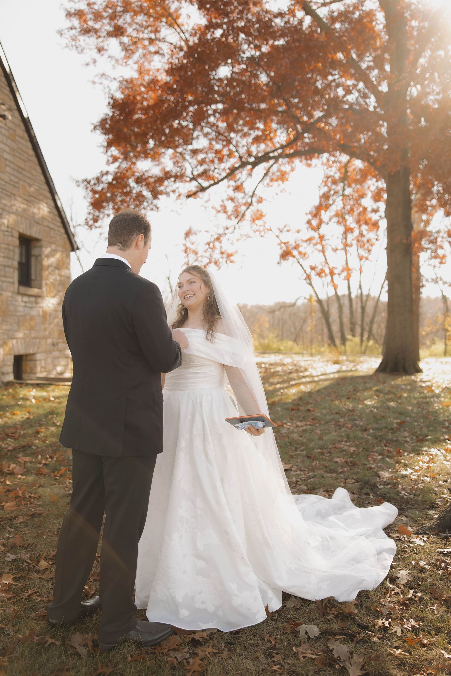 Autumn wedding photoshoot with fallen leaves and golden sunlight filtering through trees.