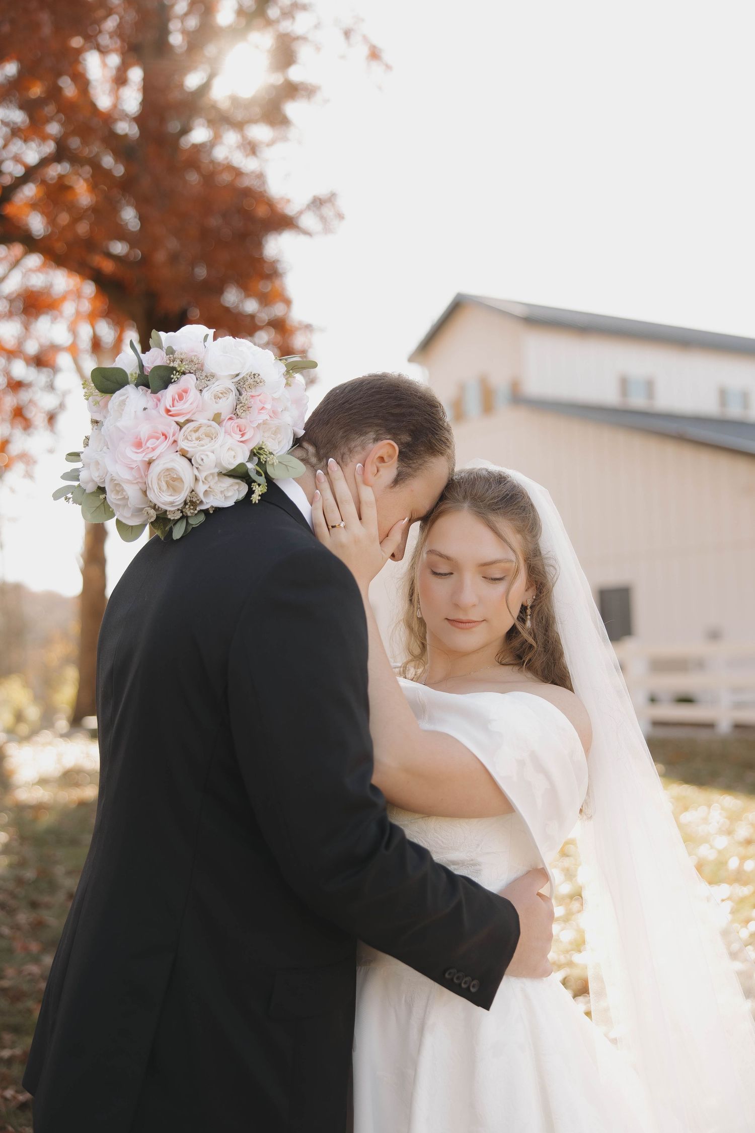 Romantic wedding couple shares intimate moments during sunset photoshoot with autumn foliage in background.