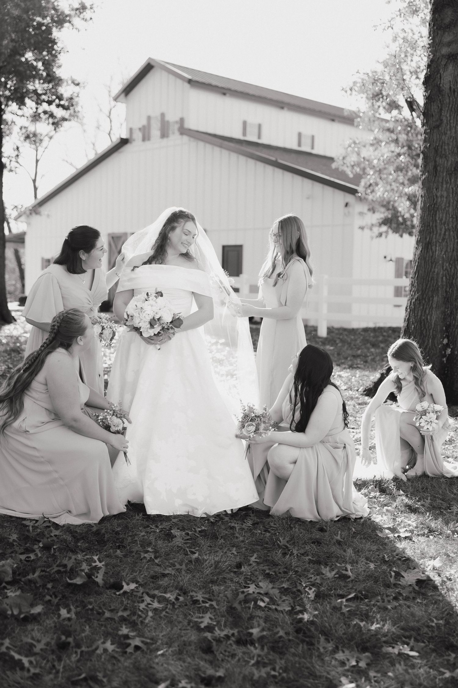 Wedding party gathered outside white barn on autumn day in black and white photograph.