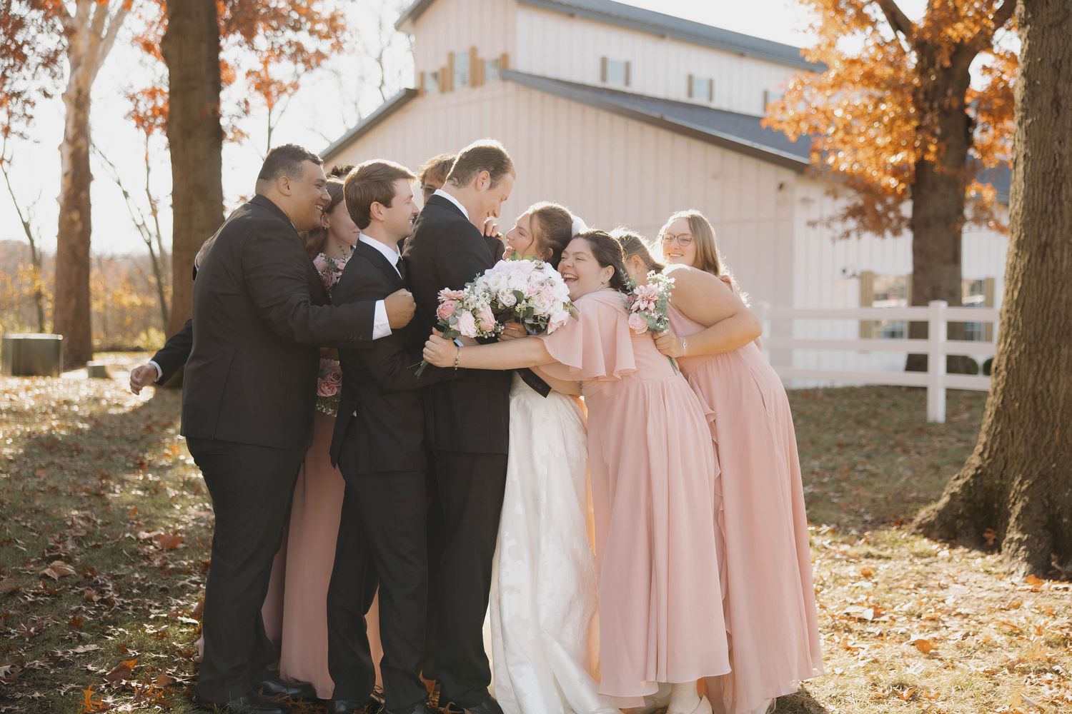 Wedding party poses together outdoors on a fall day with bridesmaids in pink dresses.